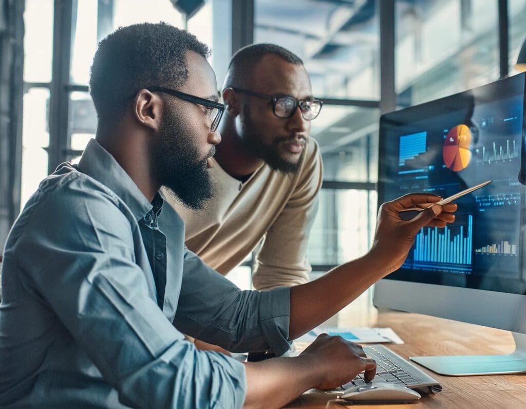 Two marketers analyzing data on a computer screen with charts and graphs displayed