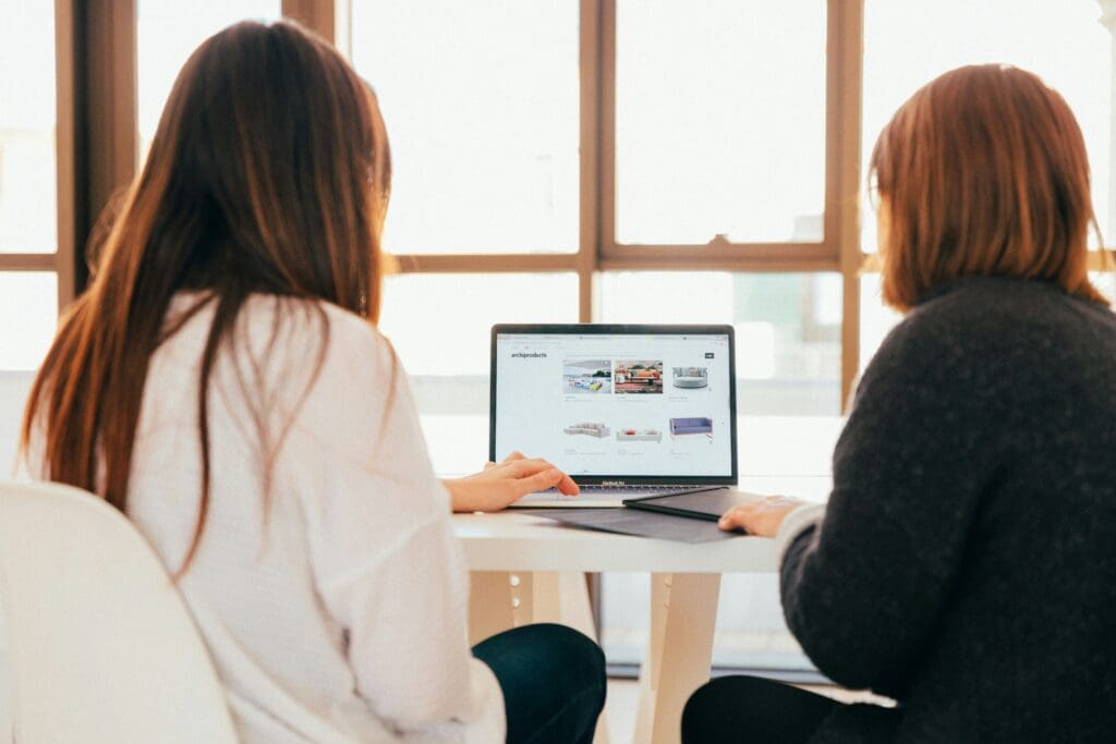 Two women sitting in front of a laptop, browsing a website